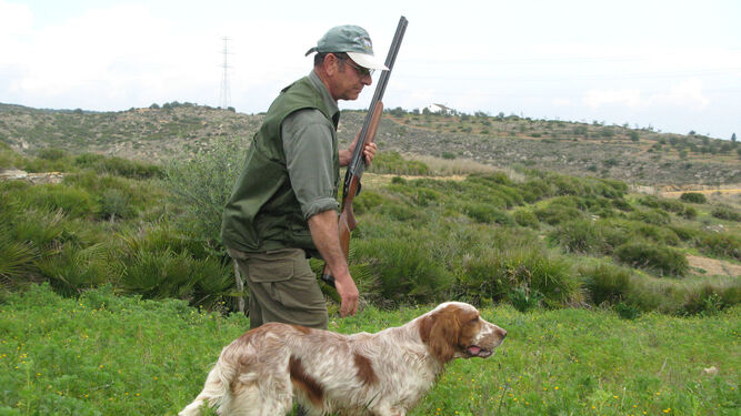 Un cazador avanza por una finca junto a su perro.