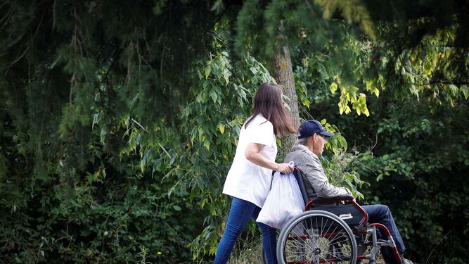 Una mujer pasea a un hombre en silla de ruedas.