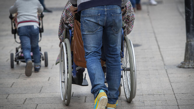 Una persona empuja la silla  de ruedas de una persona mayor.