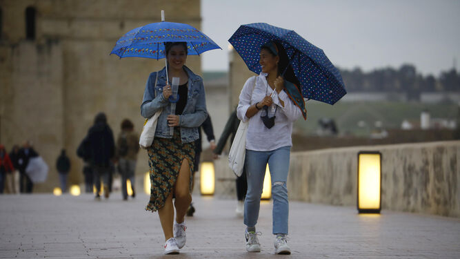 Dos jóvenes en el Puente Romano de Córdoba en un día de lluvia.
