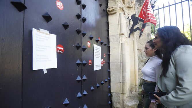 Dos personas leen los carteles pegados en la puerta del Alcázar que anuncian la huelga.