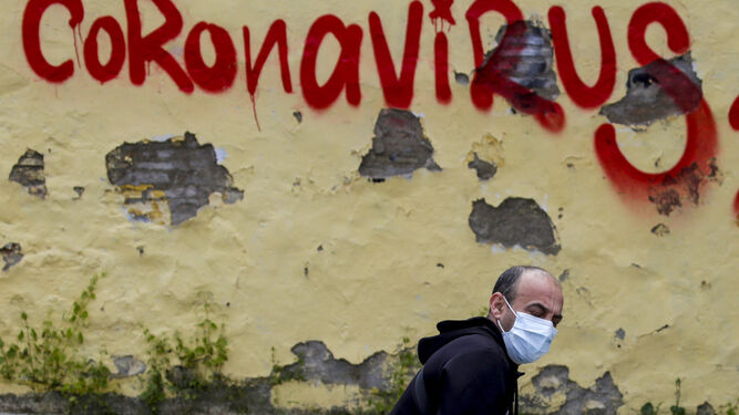 Un hombre atraviesa una fachada con una pintada en homenaje al coronavirus.