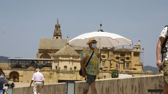 Un hombre pasea por el Puente Romano resguardado por una sombrilla.