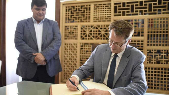 El embajador británico firma en el libro ante la mirada del alcalde de Huelva.