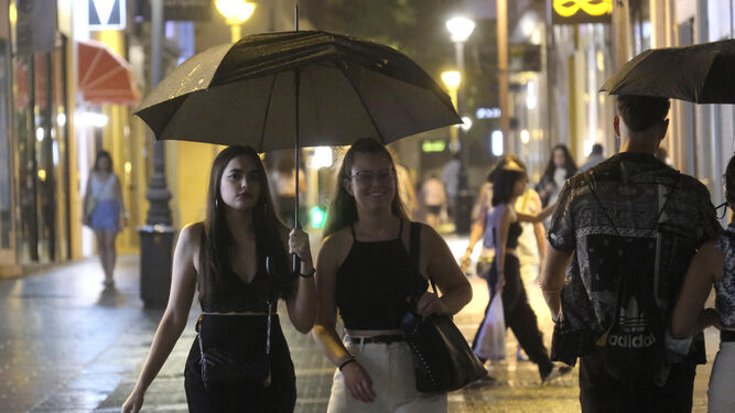 Unas jóvenes por el centro de Córdoba bajo un paraguas.
