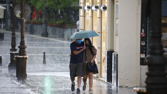 Dos personas se protegen de la lluvia con un paraguas por una calle del Centro de la capital.