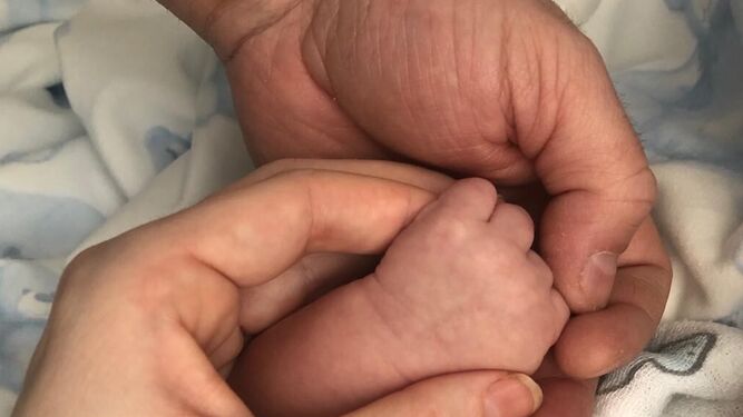 Unos padres cogen la mano de su bebé recién nacido.