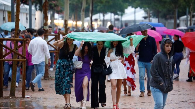 Varias jóvenes se resguardan de la lluvia bajo un plástico en la Feria de Córdoba.