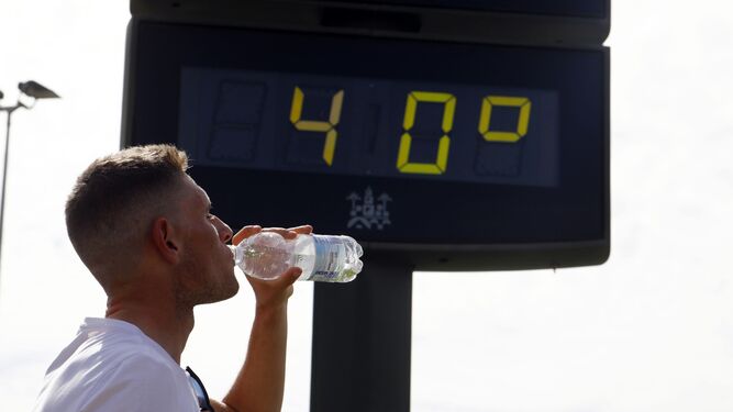 Un hombre bebe agua de una botella delante de un termómetro con 40 grados.