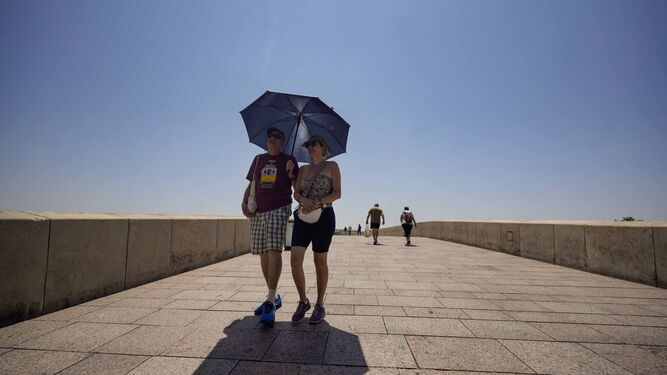 Dos personas pasan por el Puente Romano de Córdoba bajo un paraguas para resguardarse del sol.