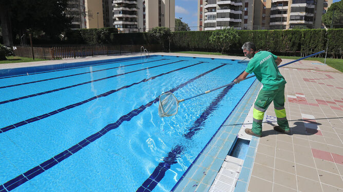 Un operario limpia el agua de una piscina de una urbanización.