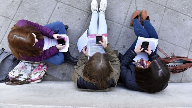Tres alumnas consultan sus teléfonos móviles en un centro educativo.
