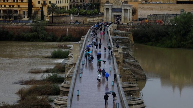 Decenas de personas cruzan el Puente Romano sobre un río Guadalquivir crecido.