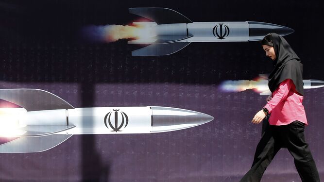 Una mujer camina junto a una pancarta antiisraelí con imágenes de misiles iraníes en Teherán.